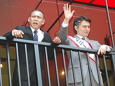 （左より）声援に応えるオバマ大統領（松下アキラ）とロムニー候補（福本ヒデ）