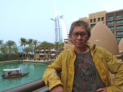 ドバイが誇る7ツ星ホテル「ブルジュ・アル・アラブ」をバックにアラビアンナイトな空間にたたずむ三池崇史監督